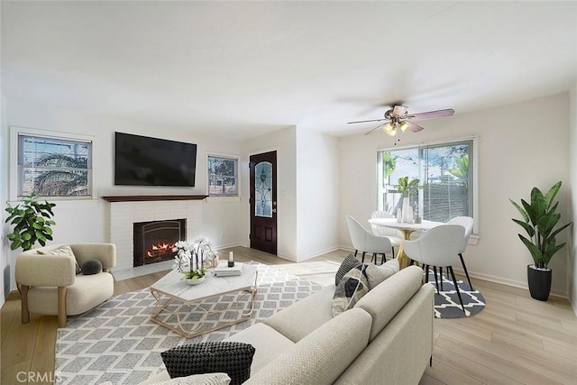 living room featuring light wood-type flooring, ceiling fan, and a brick fireplace