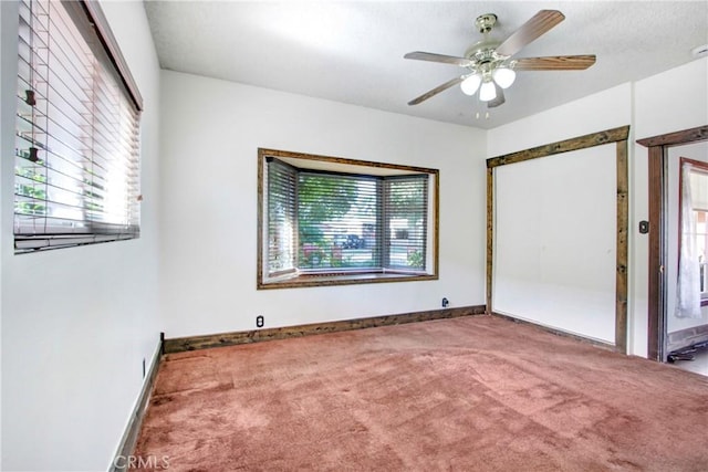 carpeted empty room featuring baseboards and a ceiling fan