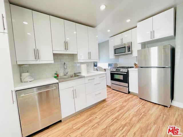 kitchen featuring backsplash, sink, white cabinetry, light wood-type flooring, and appliances with stainless steel finishes