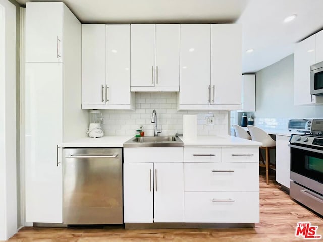 kitchen featuring stainless steel appliances, backsplash, white cabinets, light hardwood / wood-style flooring, and sink