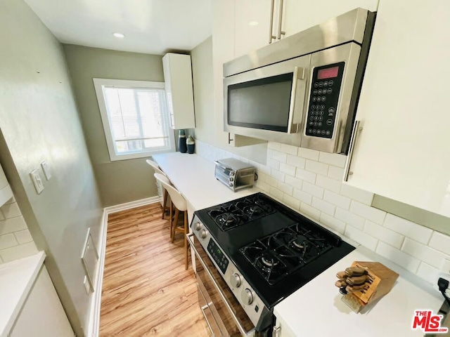 kitchen with light wood-type flooring, decorative backsplash, appliances with stainless steel finishes, and white cabinetry