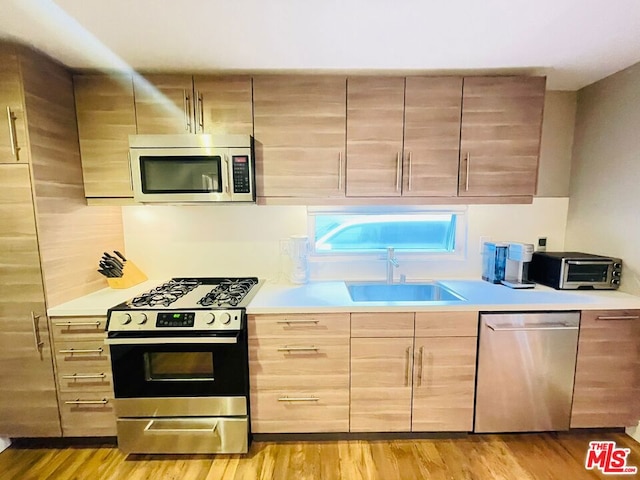 kitchen with appliances with stainless steel finishes, sink, light brown cabinets, and light hardwood / wood-style floors