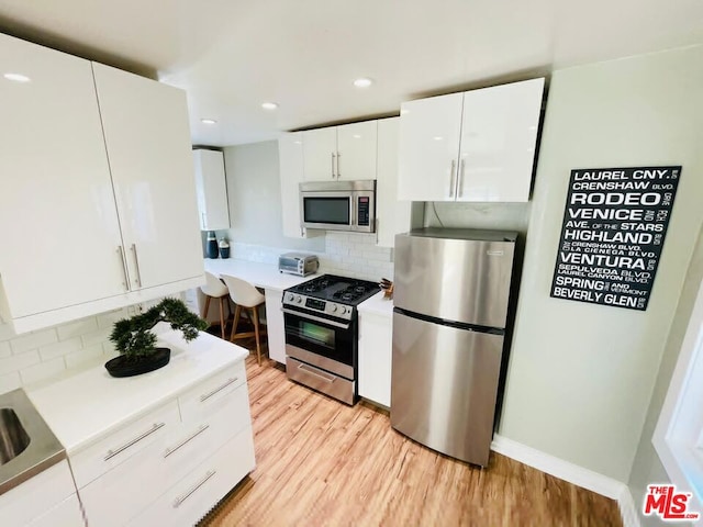 kitchen featuring light wood-type flooring, stainless steel appliances, decorative backsplash, and white cabinets