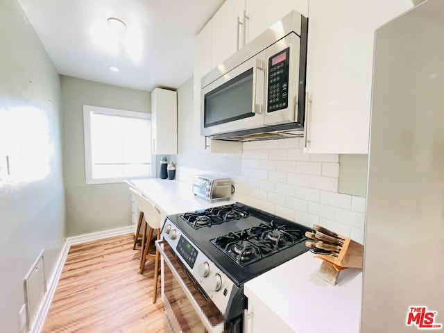 kitchen with white cabinets, appliances with stainless steel finishes, light hardwood / wood-style flooring, and tasteful backsplash