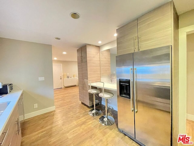 kitchen featuring light hardwood / wood-style floors, light brown cabinetry, high end refrigerator, and a breakfast bar area