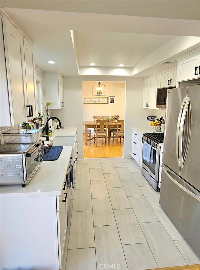 kitchen with appliances with stainless steel finishes, a raised ceiling, white cabinetry, and sink