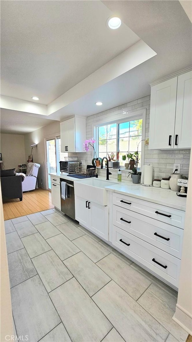 kitchen with dishwasher, white cabinetry, tasteful backsplash, sink, and a tray ceiling