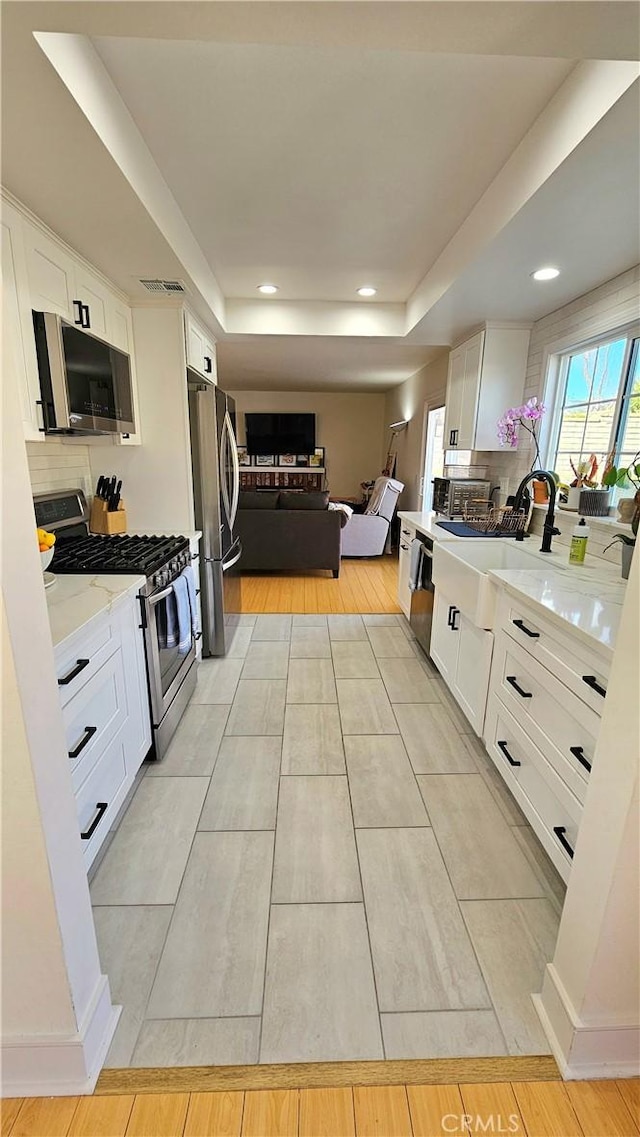 kitchen with light stone countertops, white cabinets, decorative backsplash, and appliances with stainless steel finishes