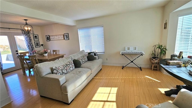 living room featuring french doors, beam ceiling, wood-type flooring, and a notable chandelier