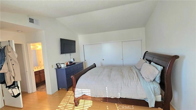 bedroom with vaulted ceiling, a closet, light hardwood / wood-style floors, and ensuite bath