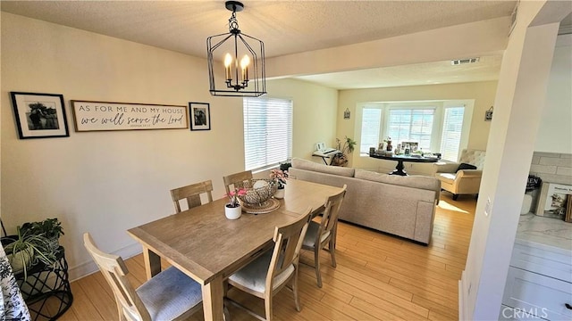 dining area featuring a textured ceiling, light hardwood / wood-style flooring, and a chandelier