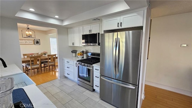 kitchen featuring decorative light fixtures, an inviting chandelier, white cabinetry, appliances with stainless steel finishes, and light stone counters