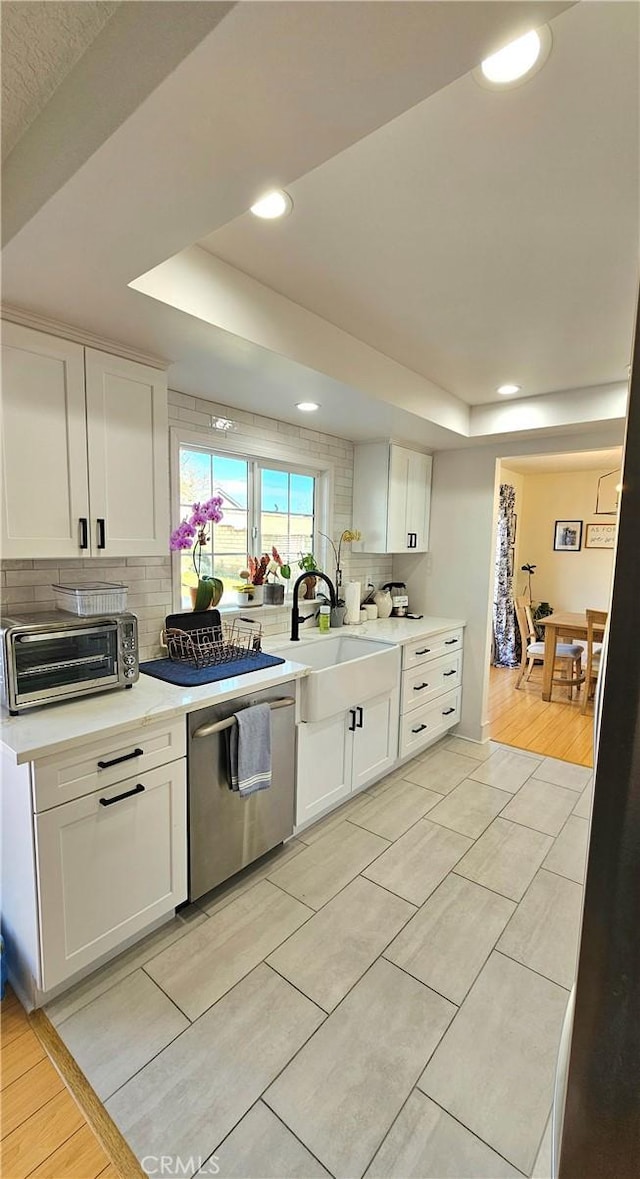 kitchen with stainless steel dishwasher, backsplash, white cabinetry, and a raised ceiling