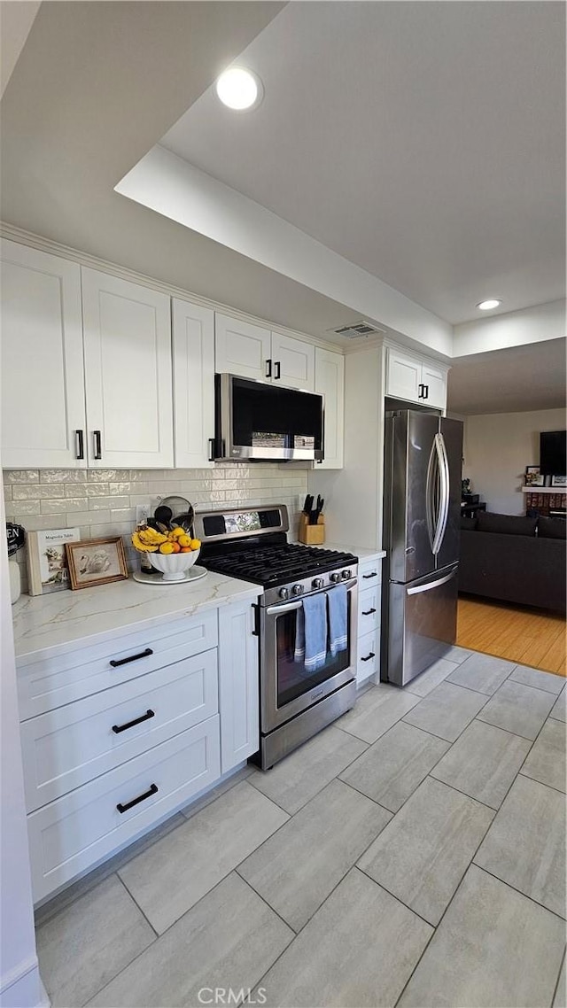 kitchen with white cabinetry, stainless steel appliances, decorative backsplash, a tray ceiling, and light stone countertops