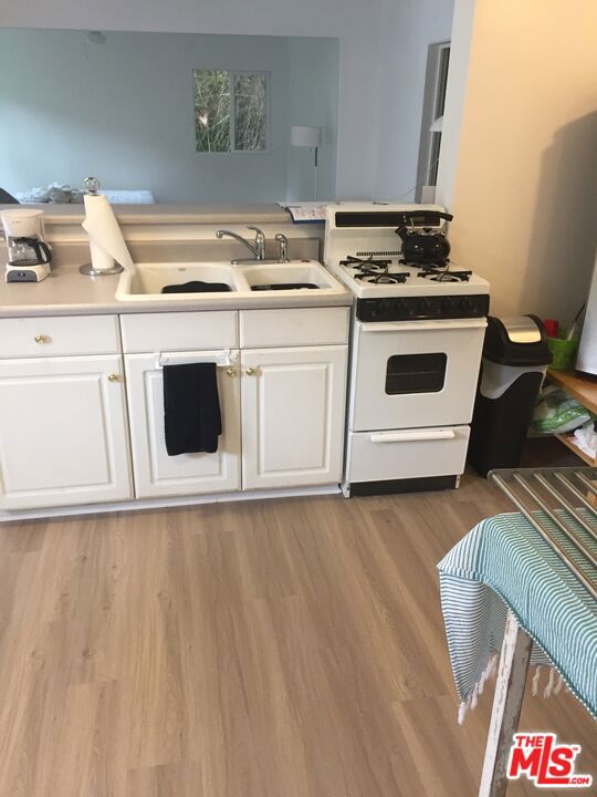 kitchen featuring white cabinetry, sink, light hardwood / wood-style floors, and white range with gas cooktop