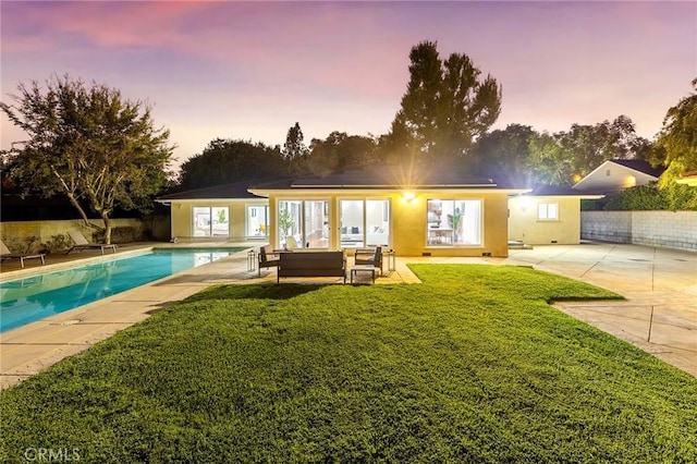 back house at dusk with a patio area, a yard, and an outdoor living space