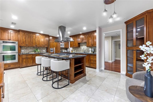 kitchen with island range hood, stainless steel appliances, hanging light fixtures, a kitchen island, and a breakfast bar