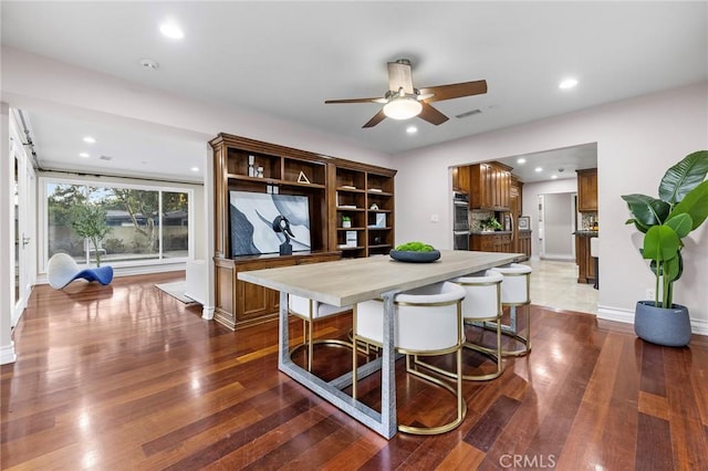 kitchen featuring ceiling fan, a kitchen breakfast bar, dark hardwood / wood-style floors, and double oven