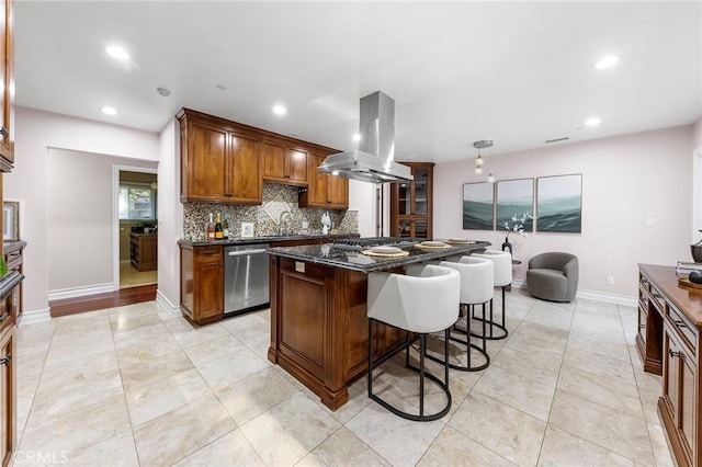 kitchen with island exhaust hood, a breakfast bar area, appliances with stainless steel finishes, dark stone countertops, and a kitchen island