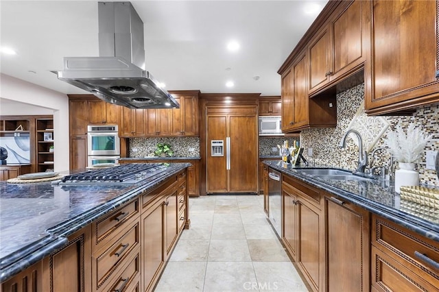 kitchen featuring island exhaust hood, appliances with stainless steel finishes, light tile patterned flooring, dark stone counters, and sink