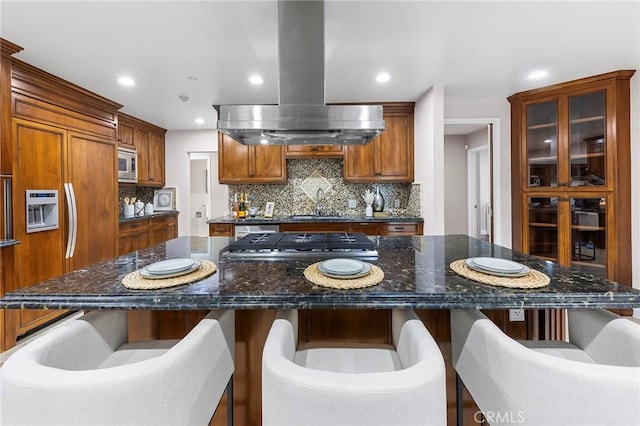 kitchen featuring island exhaust hood, built in appliances, dark stone countertops, and a large island