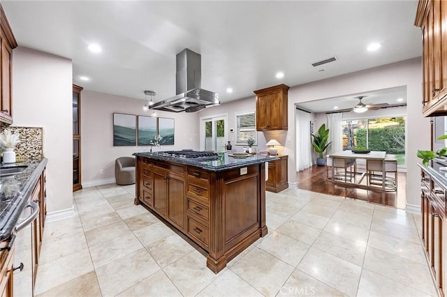 kitchen with ceiling fan, tasteful backsplash, island exhaust hood, stainless steel gas cooktop, and dark stone counters