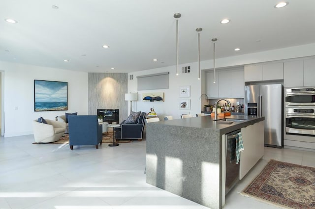 kitchen featuring appliances with stainless steel finishes, gray cabinetry, sink, hanging light fixtures, and a center island with sink