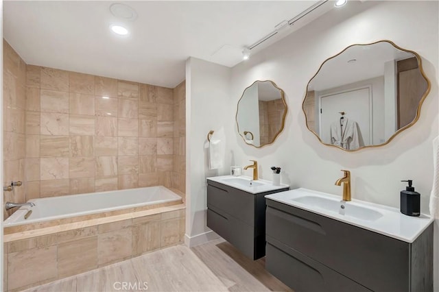 bathroom with hardwood / wood-style flooring, a relaxing tiled tub, and vanity