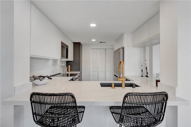 kitchen with kitchen peninsula, sink, stainless steel refrigerator, white cabinets, and range