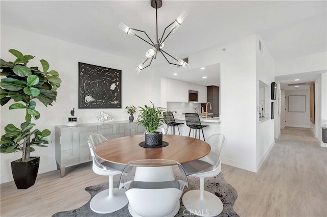 dining area with sink, a chandelier, and light wood-type flooring