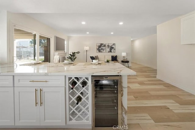 bar with light stone countertops, white cabinetry, light wood-type flooring, and wine cooler