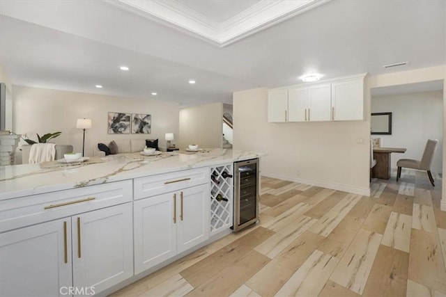 kitchen with light stone countertops, white cabinets, beverage cooler, and light hardwood / wood-style flooring