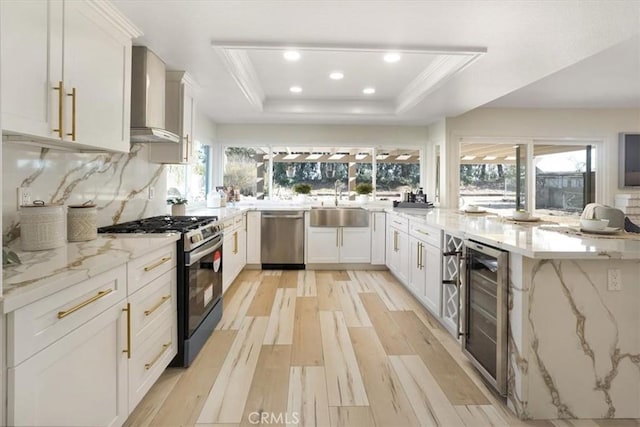 kitchen featuring white cabinetry, stainless steel appliances, a tray ceiling, beverage cooler, and light stone counters