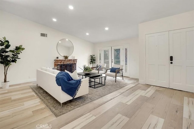 living room featuring light hardwood / wood-style floors, vaulted ceiling, french doors, and a fireplace