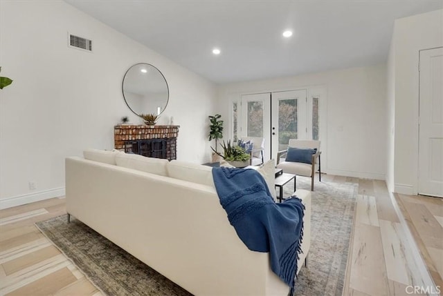 living room with a fireplace, light hardwood / wood-style floors, and french doors