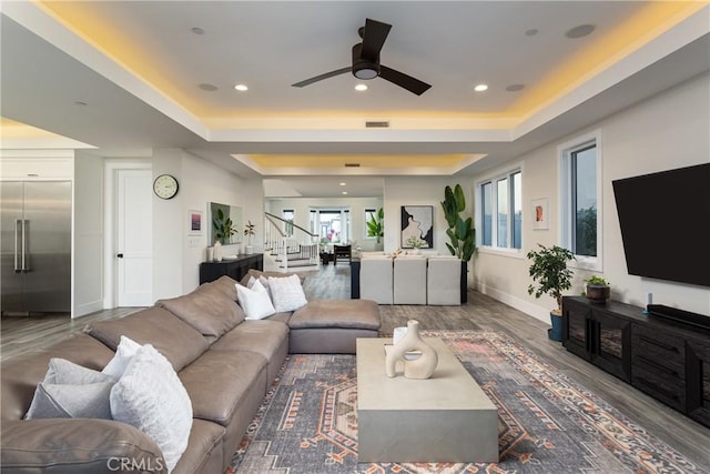 living room with hardwood / wood-style flooring, a raised ceiling, and ceiling fan