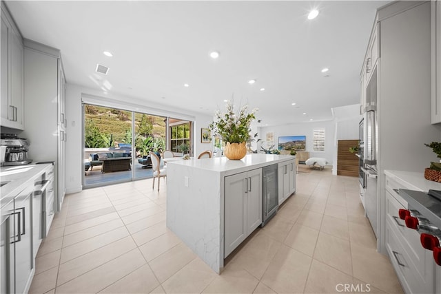 kitchen featuring a kitchen island with sink, beverage cooler, and light tile patterned flooring