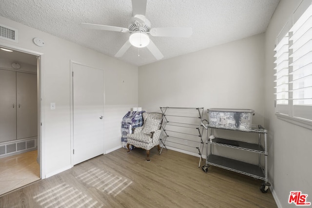 living area featuring hardwood / wood-style flooring, a textured ceiling, and ceiling fan