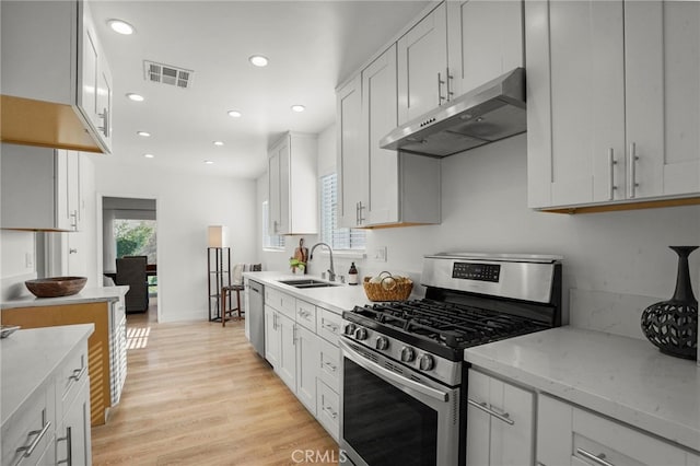 kitchen featuring light stone countertops, white cabinets, stainless steel appliances, light hardwood / wood-style floors, and sink