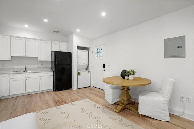 kitchen featuring black fridge, white cabinetry, stacked washer and clothes dryer, and electric panel