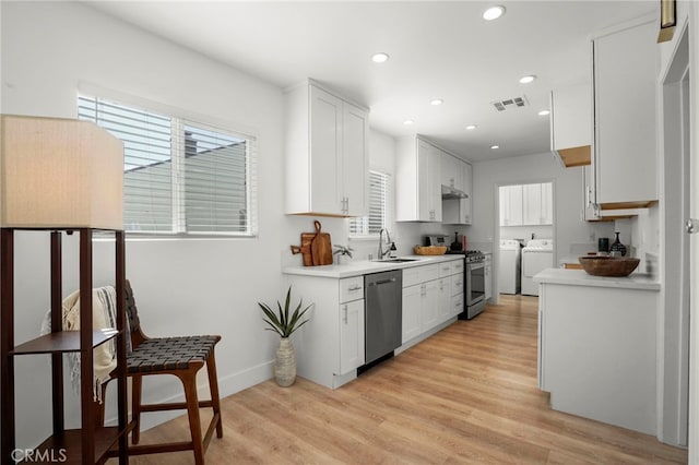 kitchen with white cabinets, appliances with stainless steel finishes, washing machine and dryer, sink, and light hardwood / wood-style flooring