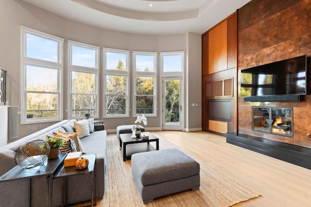 living room with light hardwood / wood-style floors, a tile fireplace, and a raised ceiling