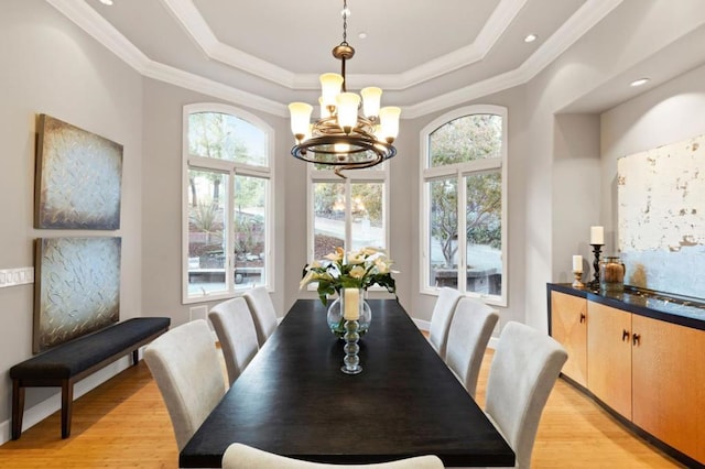 dining room with ornamental molding, a tray ceiling, a chandelier, and light wood-type flooring