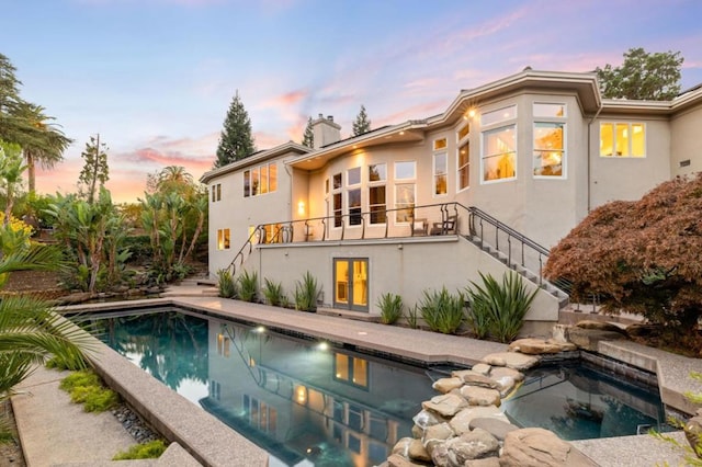 back house at dusk with a swimming pool with hot tub and a balcony