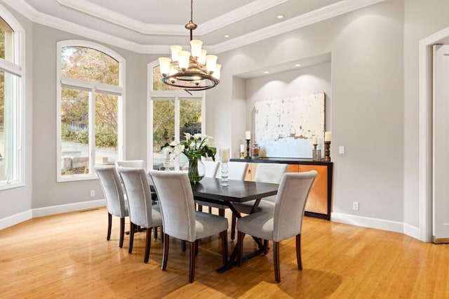 dining space featuring a notable chandelier, a tray ceiling, light hardwood / wood-style flooring, and a healthy amount of sunlight