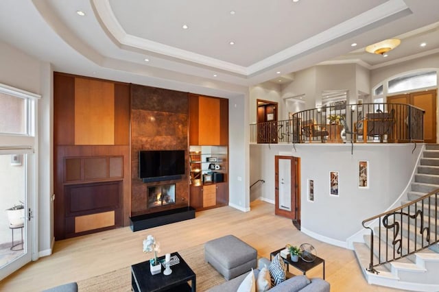 living room with a raised ceiling, ornamental molding, a healthy amount of sunlight, and light wood-type flooring