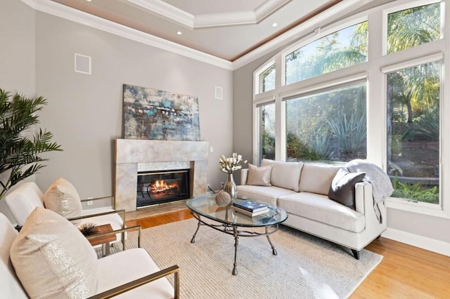 living room with a tile fireplace, ornamental molding, a wealth of natural light, and light wood-type flooring