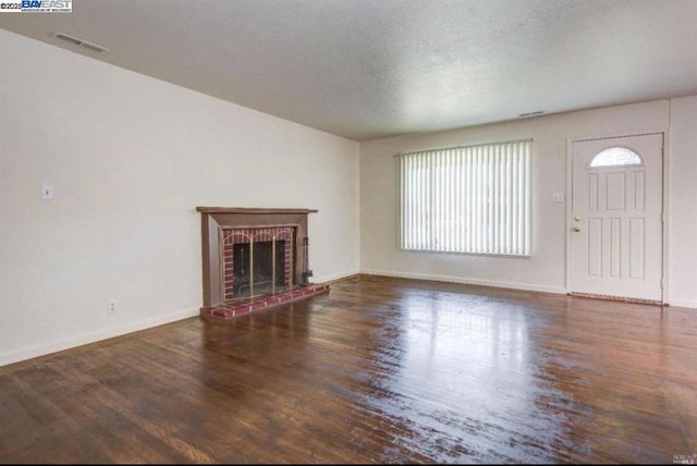 unfurnished living room with a textured ceiling, a brick fireplace, dark hardwood / wood-style flooring, and a healthy amount of sunlight