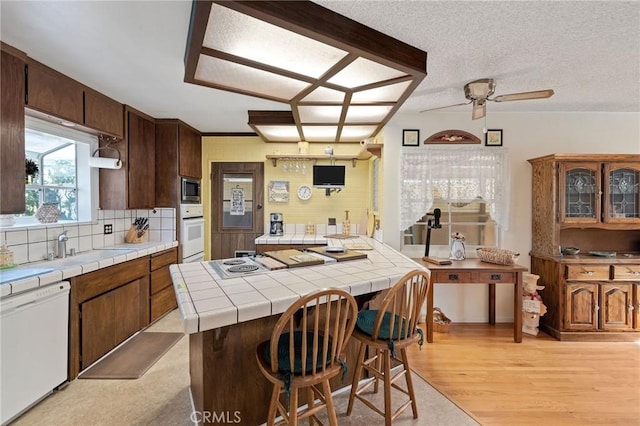 kitchen featuring tile countertops, tasteful backsplash, white appliances, a breakfast bar, and sink