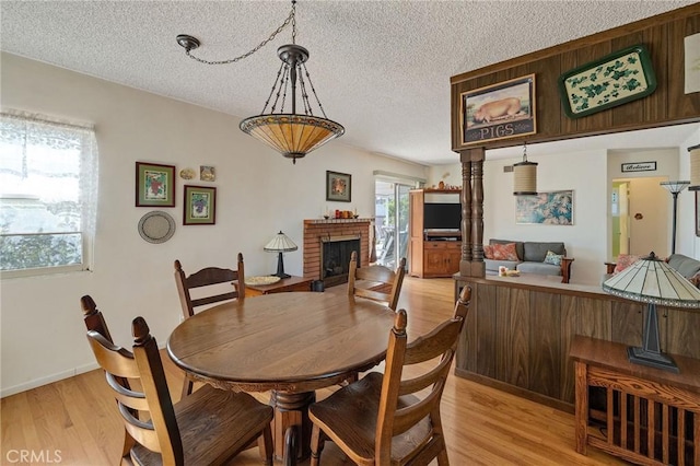 dining area featuring a brick fireplace, a textured ceiling, light hardwood / wood-style flooring, and a wealth of natural light